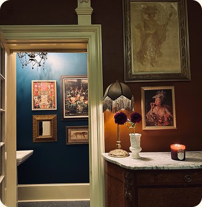 - D.WELL Lancaster, PA A hallway with a marble-topped sideboard, a fringed lamp, and framed artwork leads into a blue room with gallery-style wall decor, reflecting the tranquil aesthetic of a holistic wellness space. - D.WELL Lancaster, PA