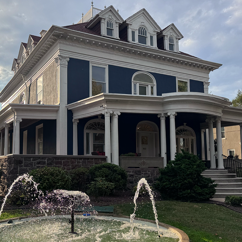- D.WELL Lancaster, PA A dark blue, two-story Victorian house for women’s wellness with a wrap-around porch, white columns, and a tiered water fountain in the front yard. - D.WELL Lancaster, PA